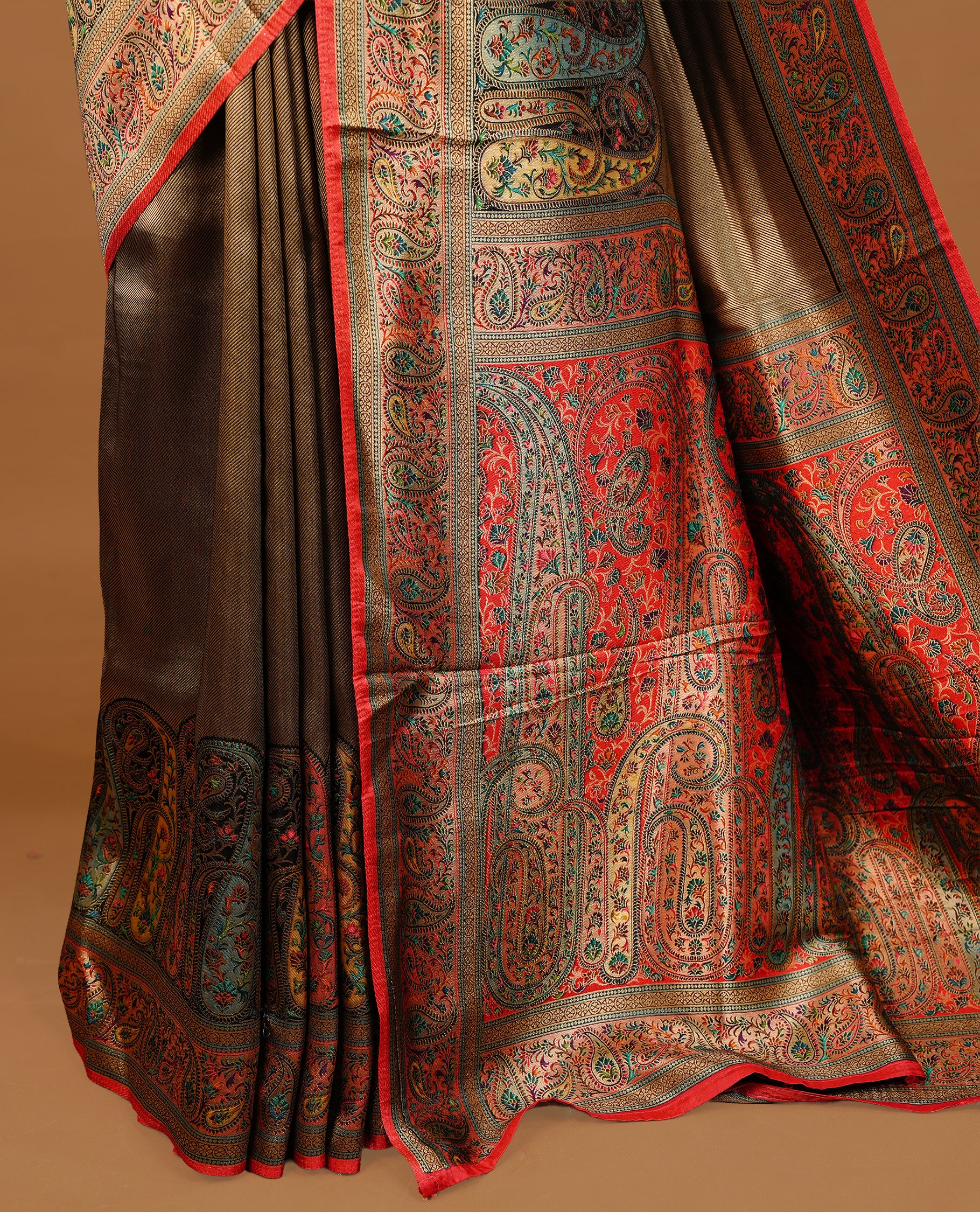 Bronze colour Pashmina Saree featuring a plain self textured body, a multicolour paisley woven border with red edging, an ornate multicolour paisley woven pallu, paired with a contrast red blouse with a matching woven border.