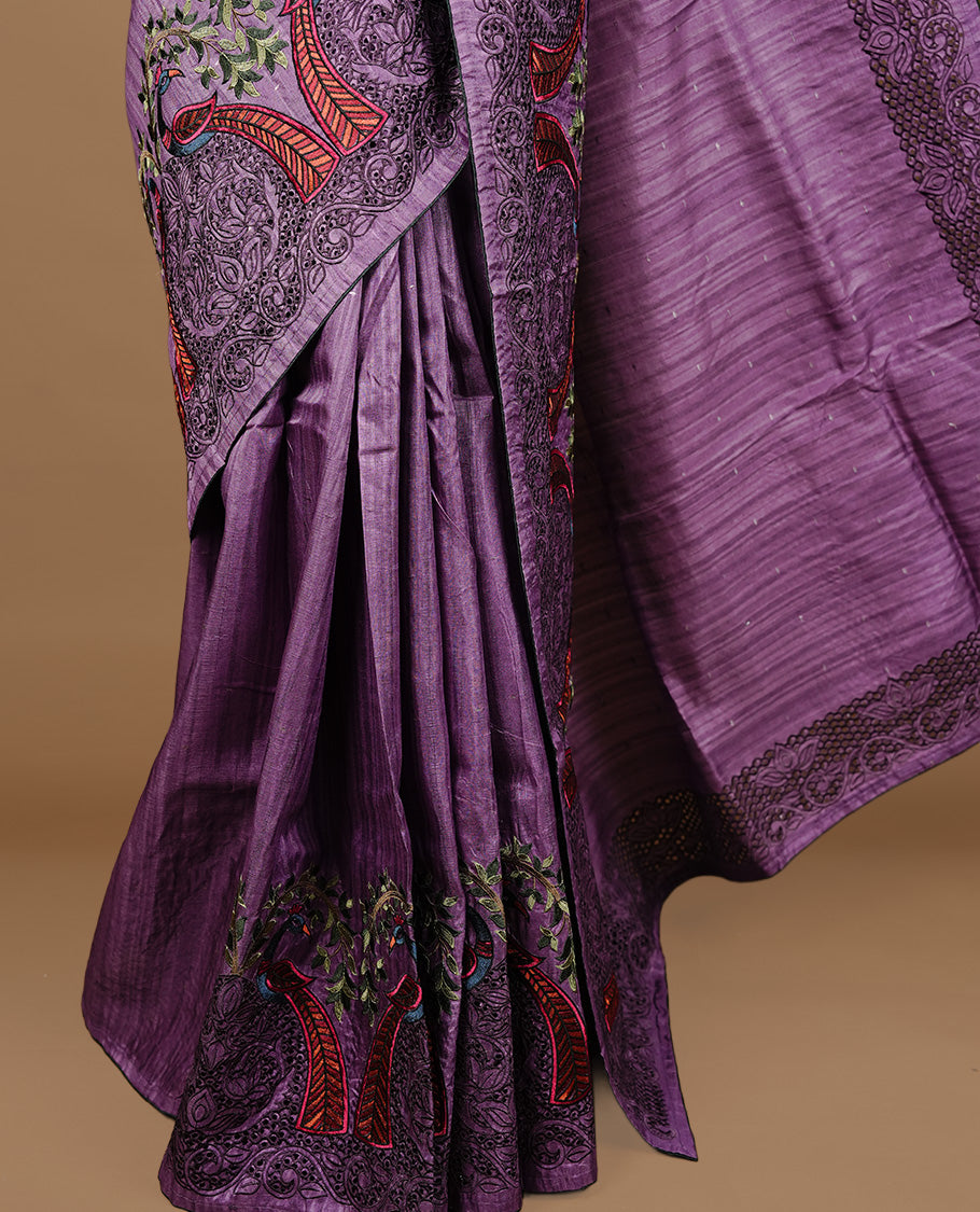 Purple colour Semi Tussar silk saree features an intricate cutwork embroidered peacock motifs on border, paired with a matching unstitched blouse piece.
