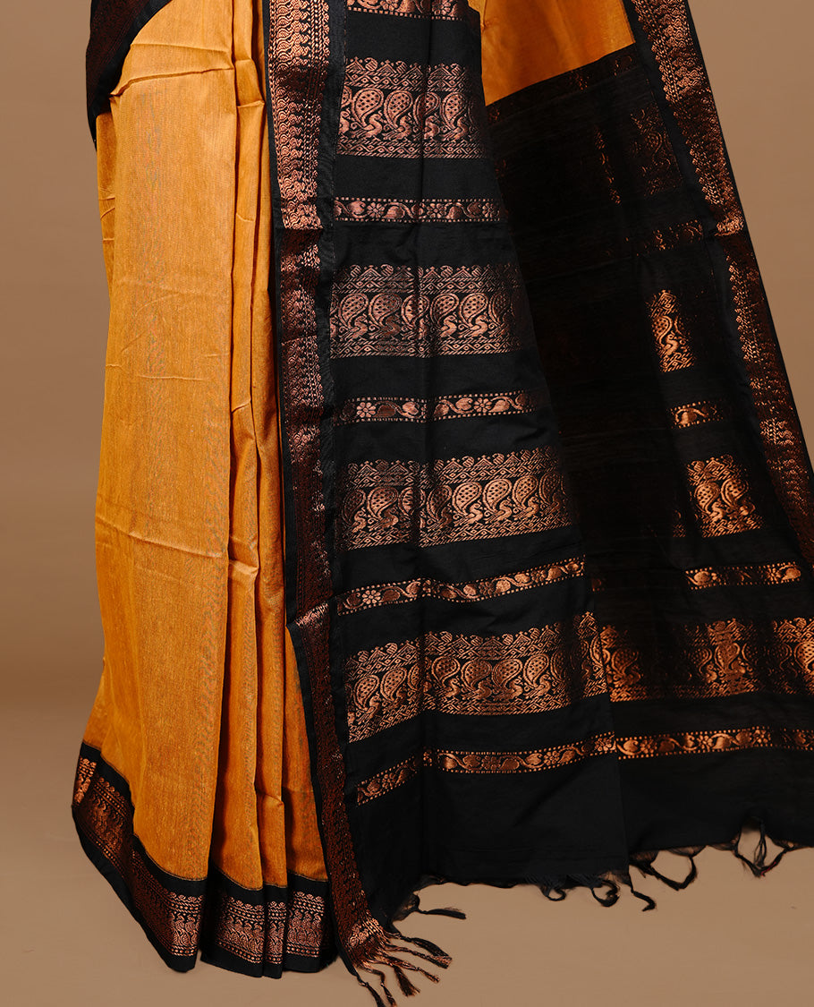 Mustard colour kalyani cotton saree featuring gold zari motifs on body, highlighting contrast Black colour with Antique gold zari border, paired with matching blouse piece.