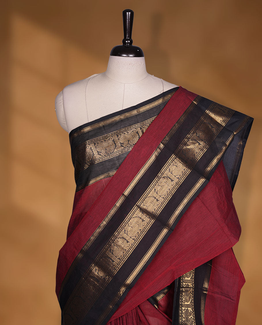 Maroon colour chettinad cotton saree featuring plain body, contrast black colour with traditional gold zari border paired with matching blouse.