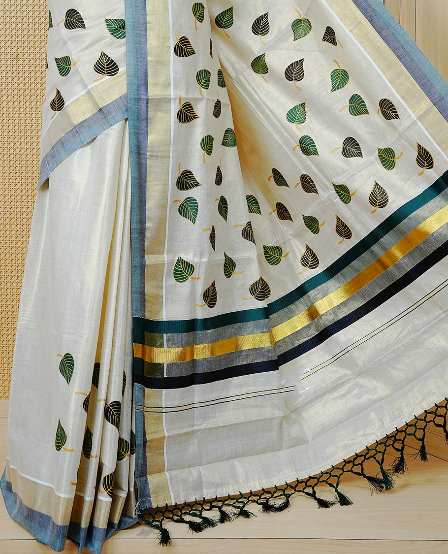 Cream Colour Tissue Kerala Saree Featuring Green and Black Leaf Prints Across the Body, Enhanced with a Gold Zari, Dark Green and Black Border & Pallu, Green  and Black Tassels, and a Matching Blouse Piece.