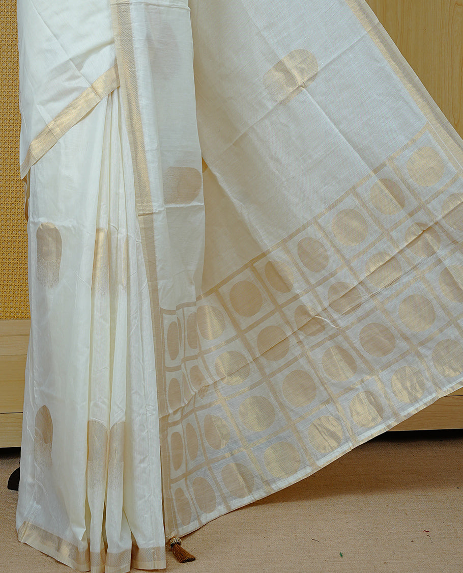 Cream Colour Organza Kerala Saree Featuring Gold Zari Buttas On The Body,  Enhanced By A  Gold Zari  Border & Geometric Design Pallu, Paired With A Matching Blouse Piece.