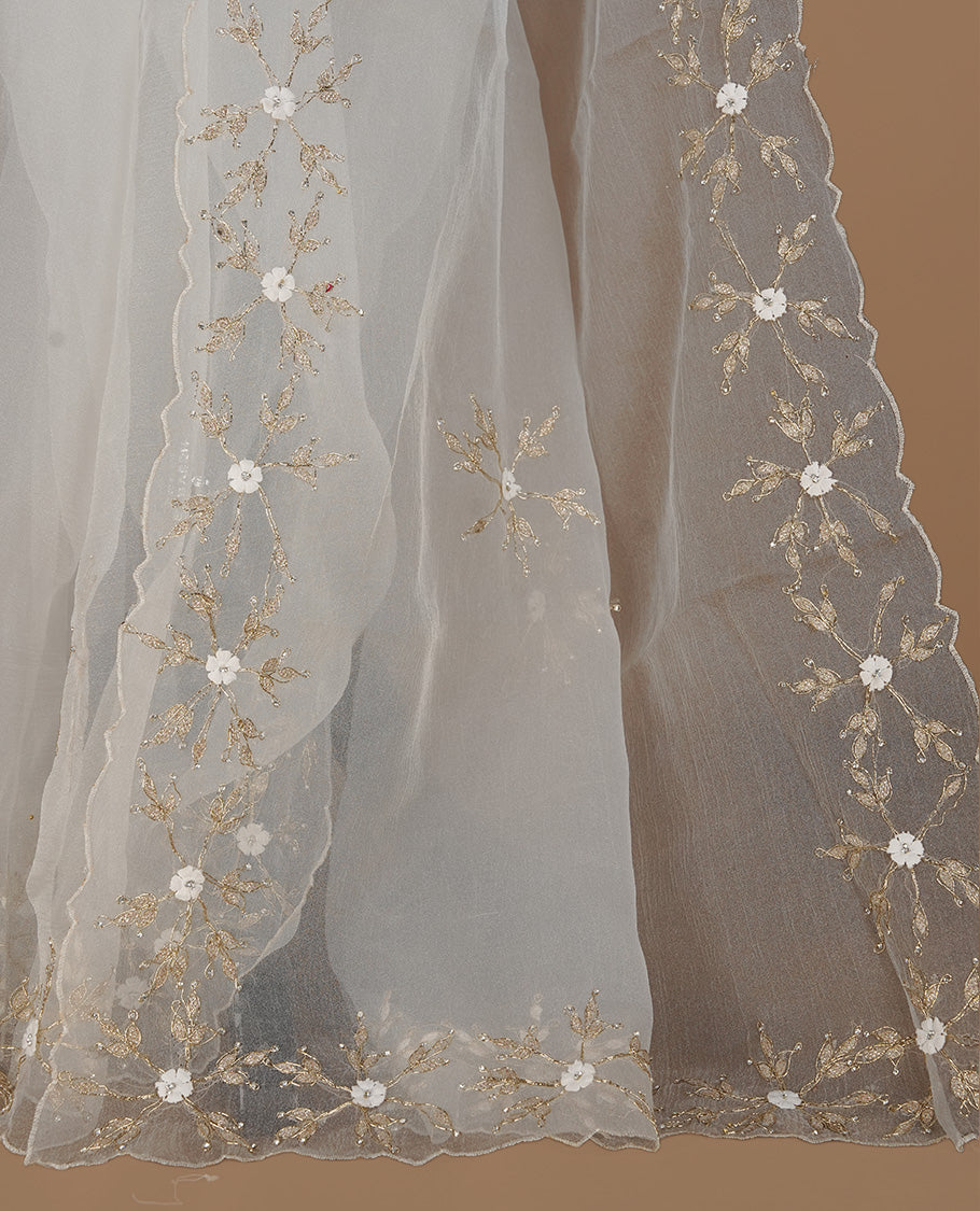 White colour crush organza saree featuring gold threan floral and stone worked body, highlighting scalp designed border, paired with matching blouse piece.