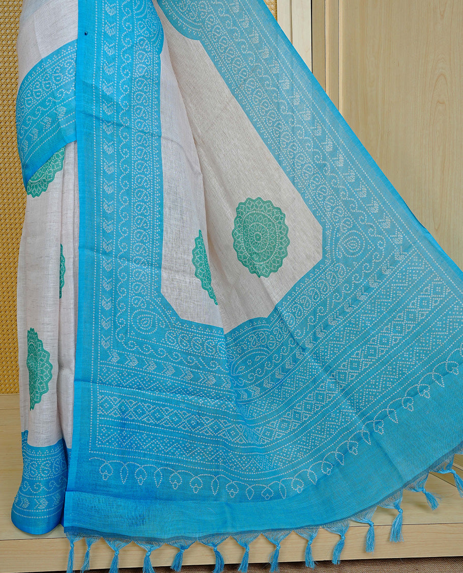 Cream colour semi linen saree featuring Green Ajrakh pattern print on body, complemented by contrast Blue colour with same pattern print border, comes with matching blouse piece.