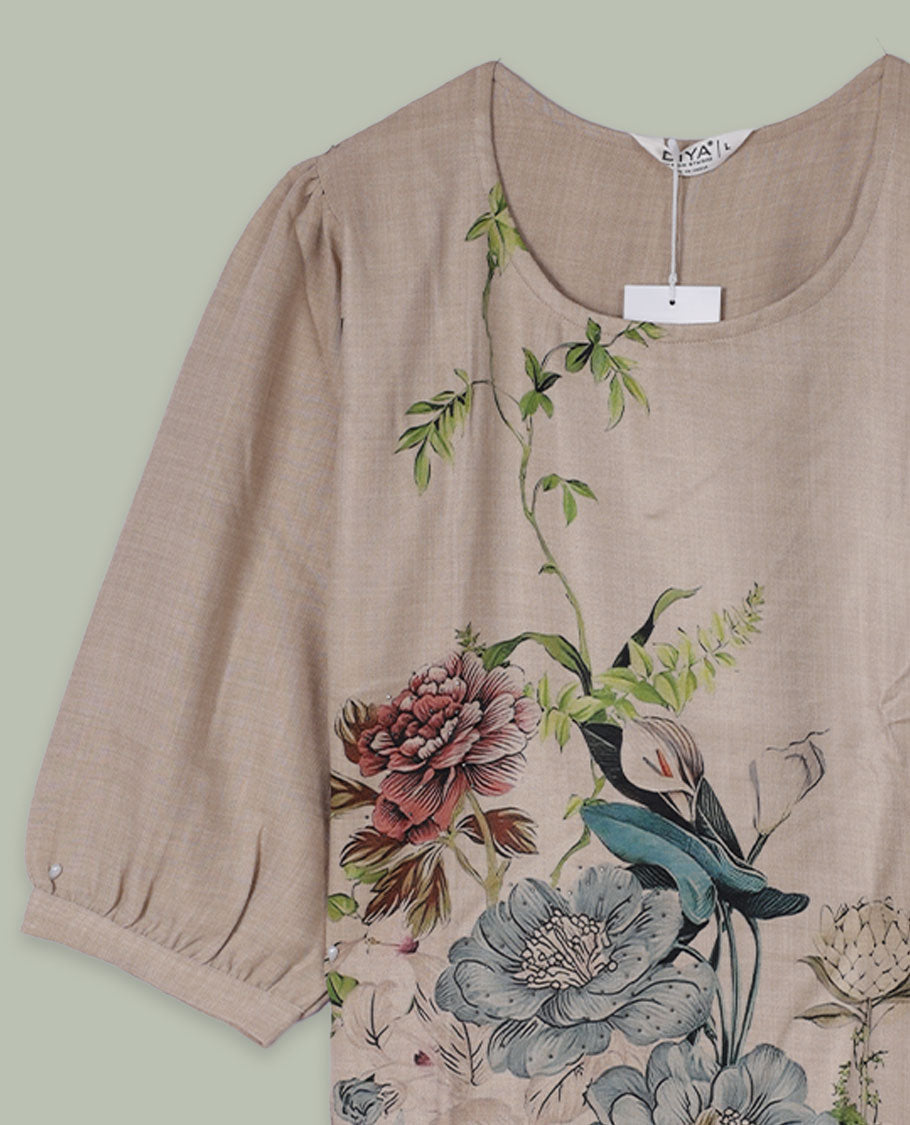 Beige round-neck top with elbow-length sleeves and placement floral print in muted blue, green, and rose tones along the front hem and side.