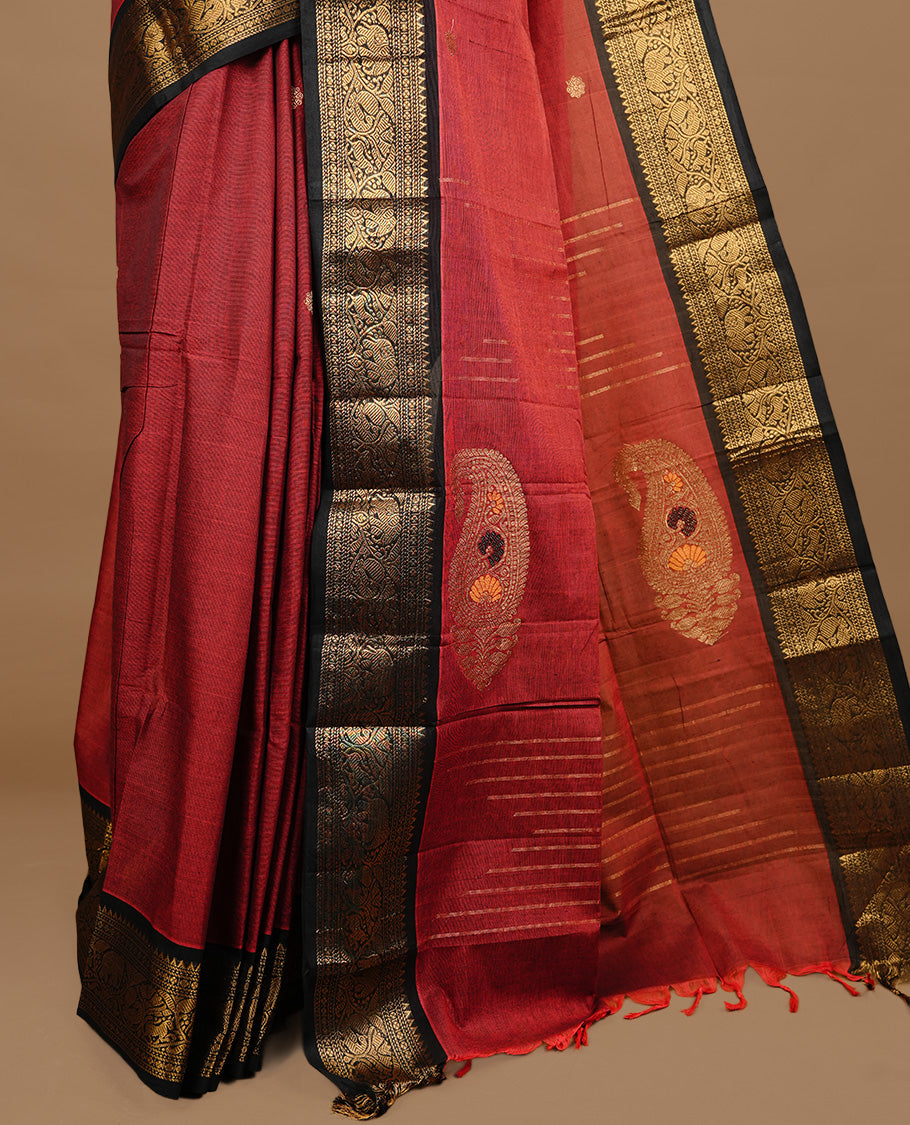 Dark red colour chettinad cotton saree featuring gold zari motifs on body, complemented by black colour with zari border, paired with matching blouse piece.