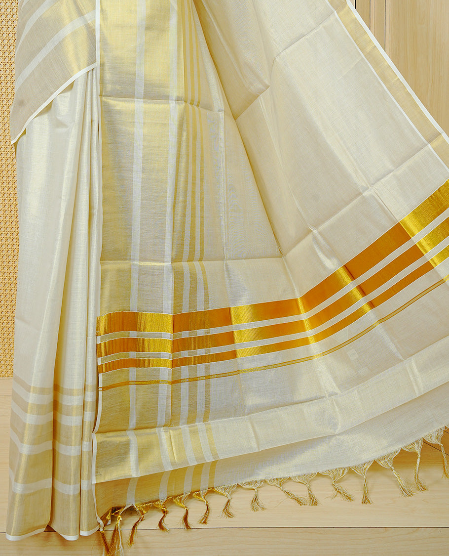 Cream Colour Tissue Kerala Saree Featuring A Classy Plain Body, Beautifully Enhanced With A Traditional Gold Zari Striped Border And Rich Gold Zari Pallu, Finished With Elegant Tassels, Paired With A Matching Blouse Piece.
