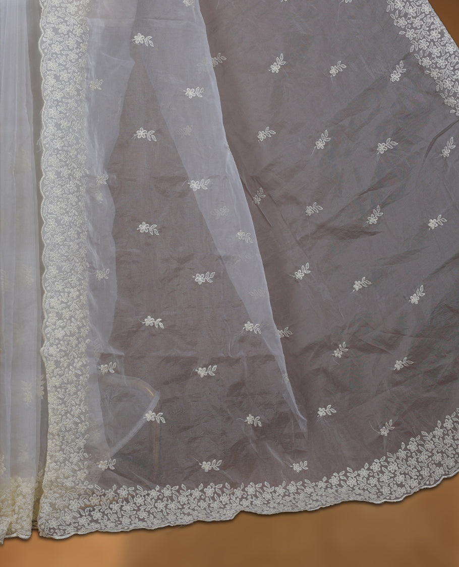 Light yellow colour organza designer saree featuring a subtle self patterned body and an intricately scalloped floral thread embroidered border all around, complemented by a coordinating embroidered pallu and paired with a matching blouse.