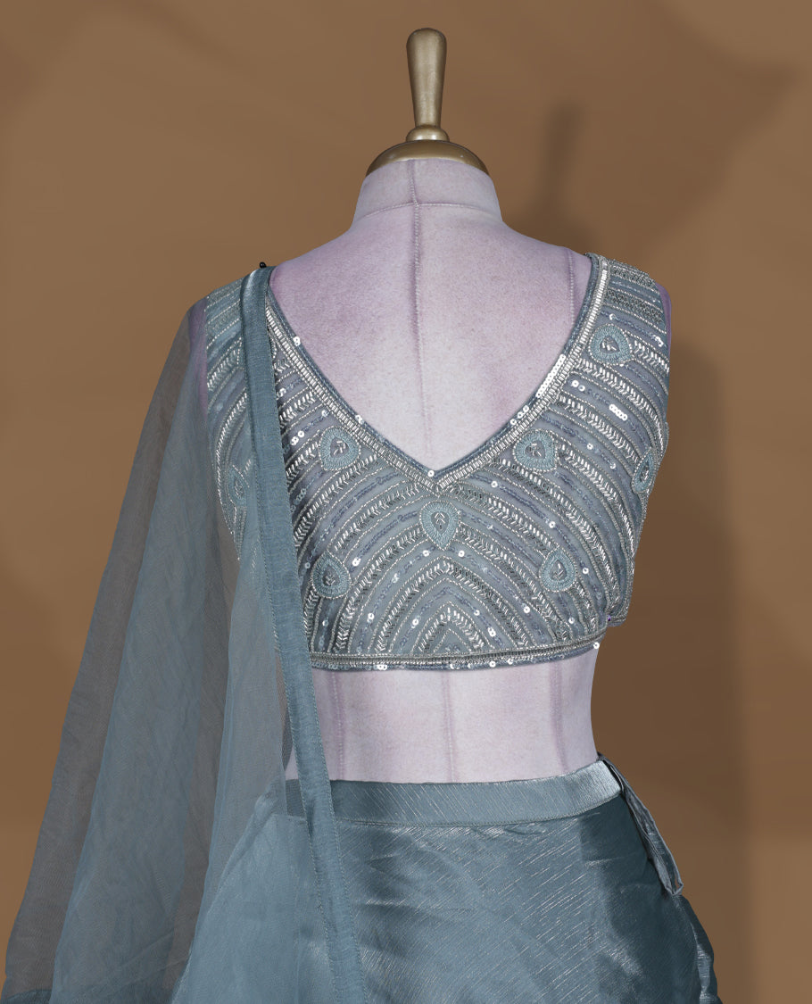 Dusty teal blue colour lehenga set with stitched sleeveless heavily embellished blouse featuring scalloped neckline, matching stitched flared lehenga, and plain sheer dupatta.