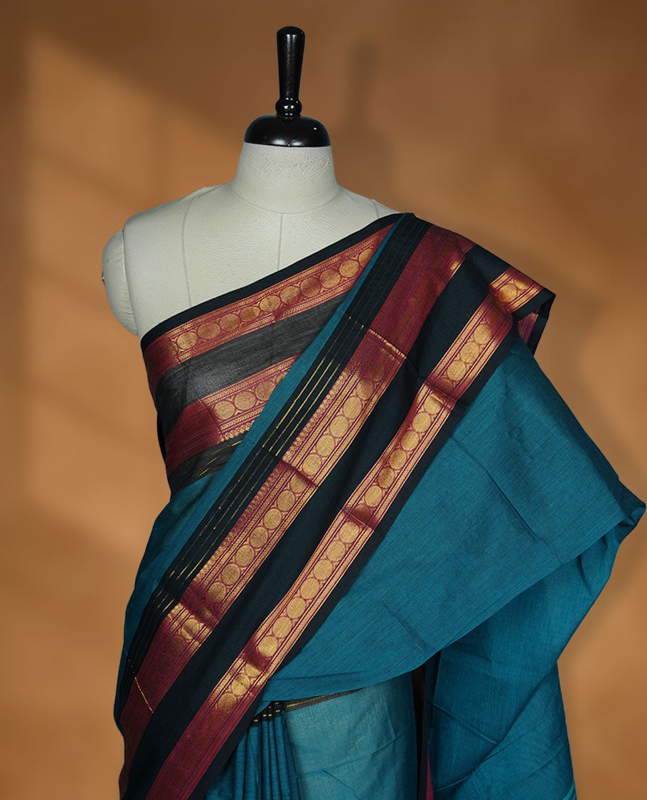 Teal colour chettinad cotton saree featuring plain body, contrast black and red colour with traditional gold zari border paired with matching blouse.