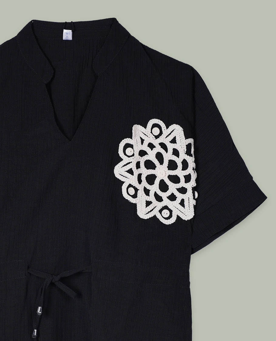 Black short-sleeve top with V-slit band neckline, contrast ivory crochet motif on one side, and adjustable drawstring detail at the waist.