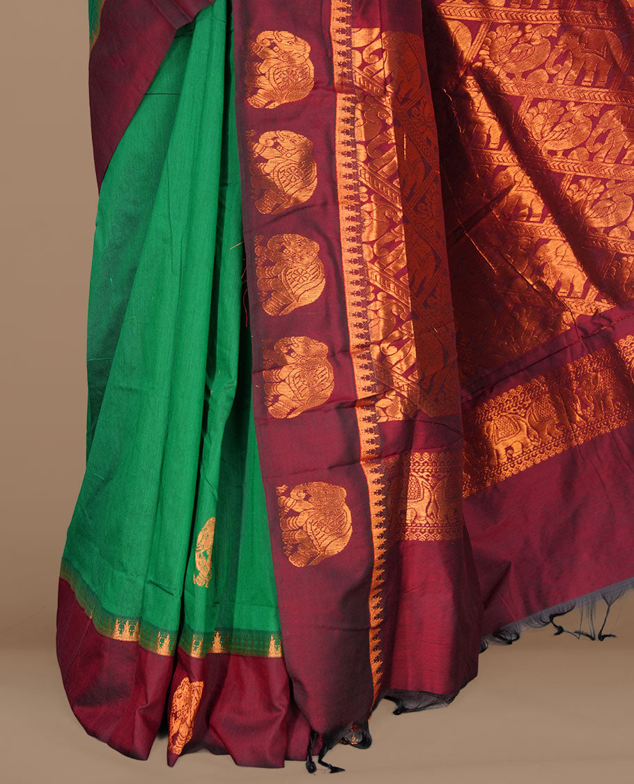 Green colour kalyani cotton saree featuring gold zari motifs on body, complemented by contrast maroon color with copper zari elephant pattern border , paired with matching blouse piece.