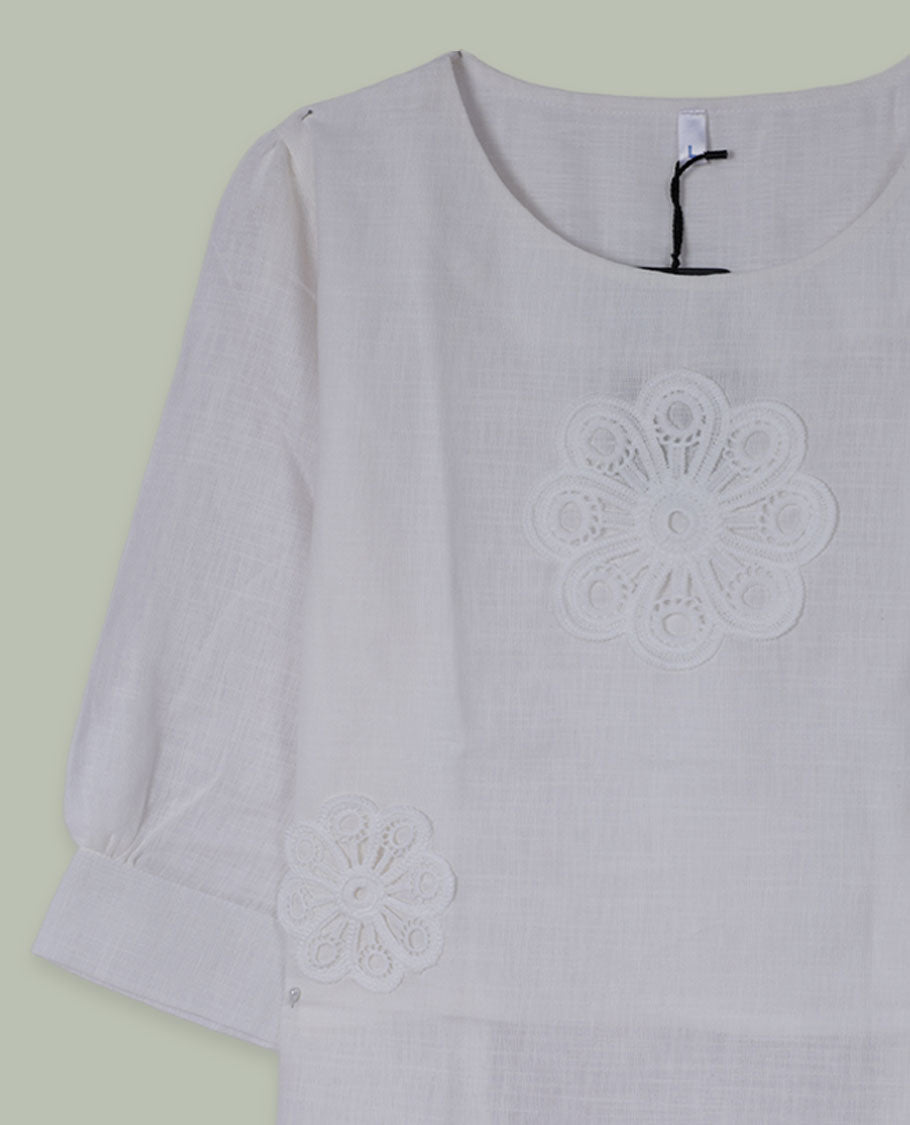 White three-quarter sleeve top with round neckline and tonal crochet floral appliqués placed at the center front and near the hem.