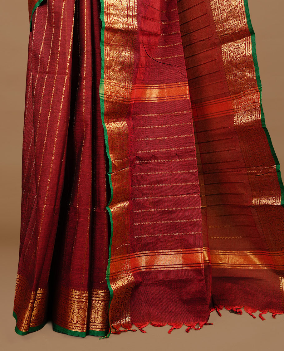 Maroon colour chettinad cotton saree featuring gold zari stripes on body, complemented by  self colour with zari green colour piping border, paired with matching blouse piece.