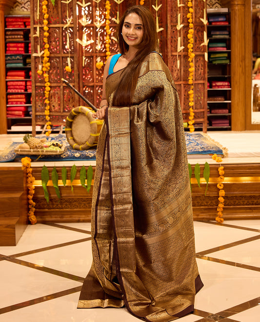 Dark chocolate colour Kancheepuram silk saree featuring intricate gold zari geometric and floral weaving throughout, completed with a rich gold zari border and grand pallu, paired with a matching blouse
