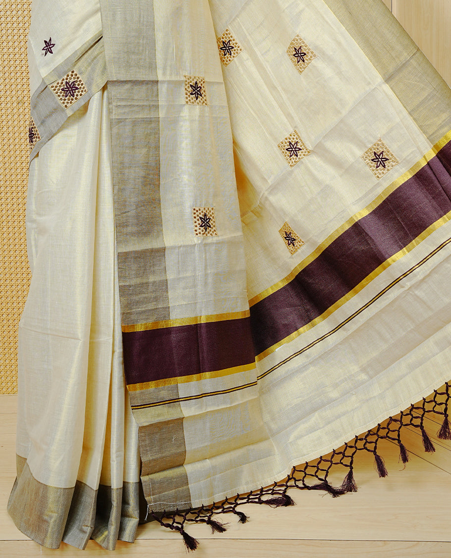 Cream Colour Tissue Kerala Saree Featuring Delicate Maroon Floral Embroidery Work Across The Body, Enhanced With A Light maroon Zari Border And A Rich Maroon & Gold Zari Pallu, Finished With Maroon Tassels And A Matching Blouse Piece