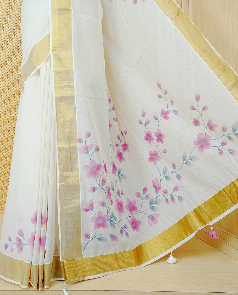 Cream Colour Cotton Kerala Saree Featuring Digital Pink Floral Prints Across The Body, Enhanced With A Gold Zari Border, Traditional Gold Zari Pallu, Finished With Pink & White Tassels And A Matching Blouse Piece