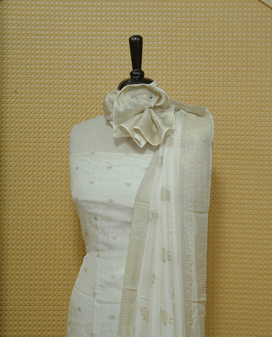 Cream colour Salwar material featuring gold zari Buttas on body, paired with matching dupatta & Bottom.