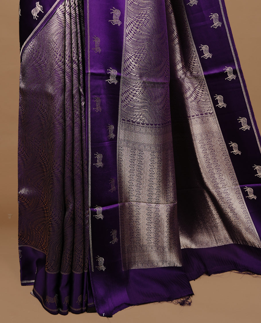 Purple colour semi Banaras crepe silk saree featuring an elegant gold zari patterned body, highlighted by a plain border adorned with traditional gold zari cow motifs. Paired with a matching blouse piece.