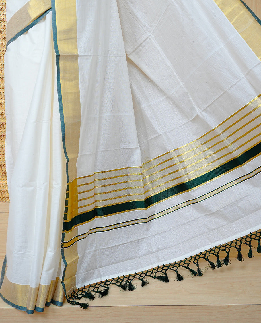 Cream Colour Cotton Kerala Saree Featuring A Plain Body, Enhanced With A Gold Zari & Green  Colour Border, A Traditional Gold Zari Pallu, Green Tassels, And A Matching Blouse Piece.