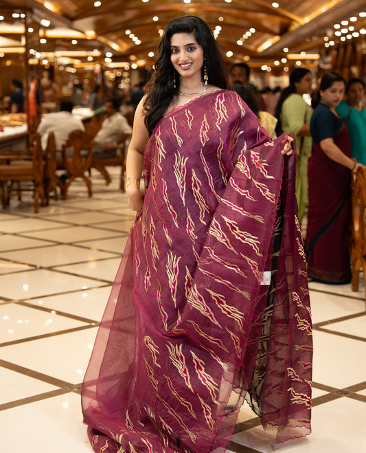 Wine colour sheer Organza saree featuring Gold thread embroidery with modern wavy & flame inspired motifs and scallop border, comes with matching organza blouse.