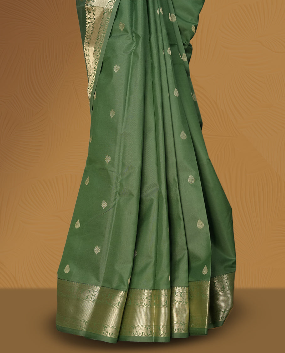 Dark pista green colour soft silk saree adorned with small golden buttas, enhanced by a shimmering gold zari border and pallu with delicate motifs & Paired with a matching blouse.