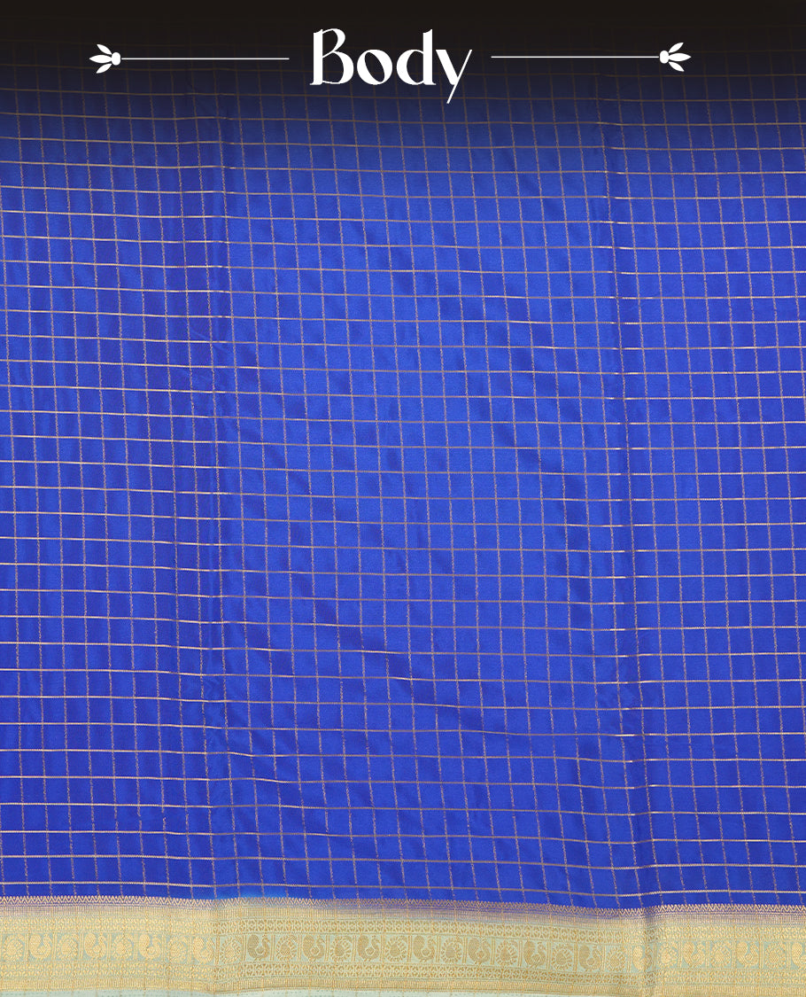 Blue colour mysore crepe saree with gold zari check pattern on body, complemented by contrast sky blue colour border featuring peacock and chakkram motifs, paired with matching blouse.