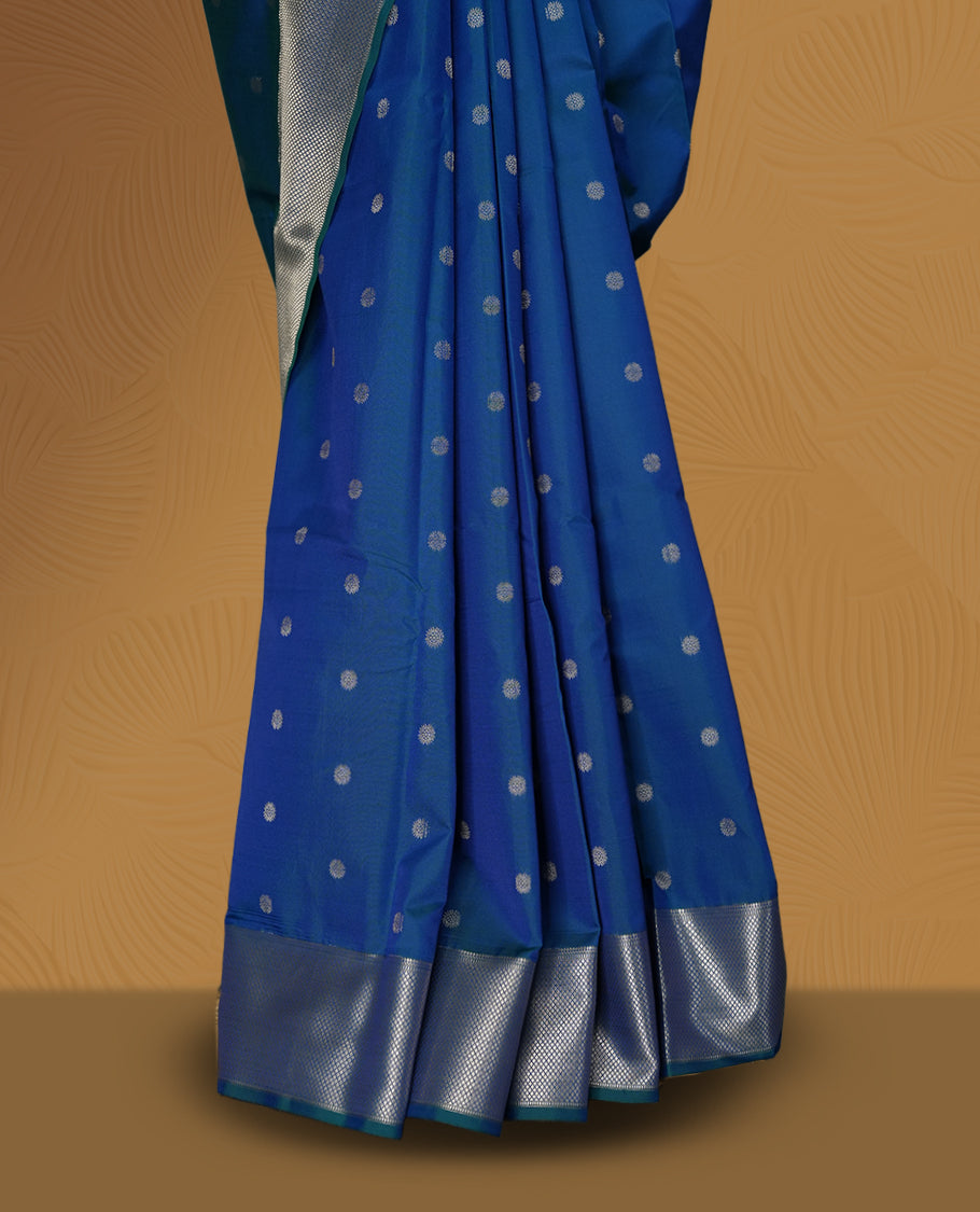 Royal blue colour soft silk saree adorned with small silver buttas, enhanced by a shimmering silver zari border and pallu with delicate motifs & paired with a matching blouse.