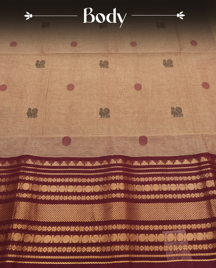 Beige Colour silk cotton saree with scattered maroon and black buttas, ornate maroon and gold zari border with geometric patterns, gold zari pallu with diamond lattice, plain beige blouse with maroon border.