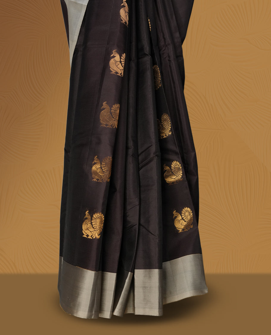 Dark brown colour soft silk saree embellished with graceful golden buttas, enhanced by an elegant silver grey border and pallu & Paired with a matching blouse.