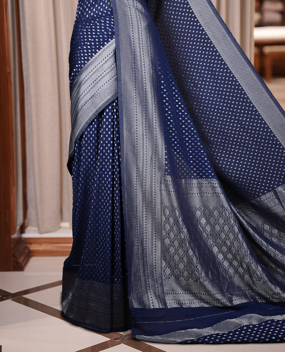 Navy blue colour Banarasi silk saree featuring intricate zari weaving and a soft silk texture, Adorned with silver motifs on the body, complemented by a rich Banarasi border and pallu & Comes with a matching blouse.