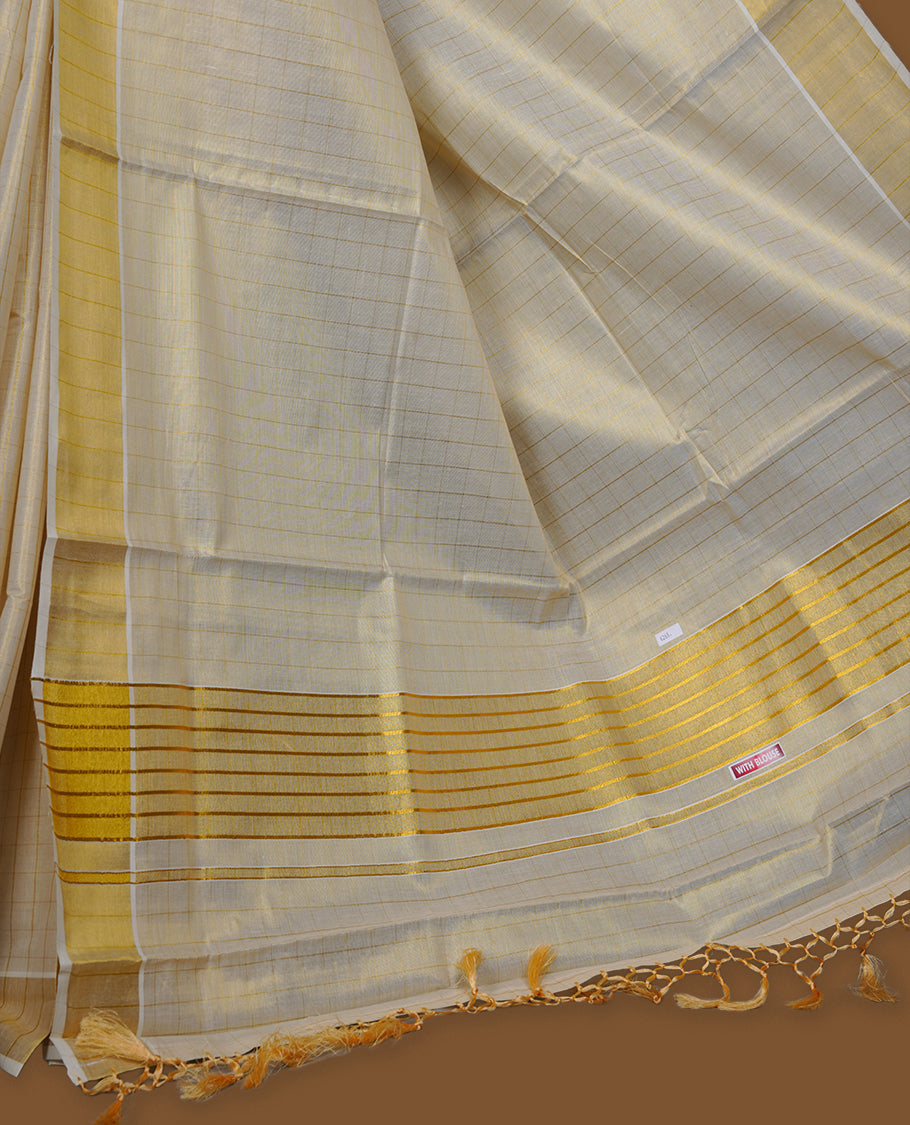 Off-white colour tissue Kerala saree with subtle gold checks across the body, finished with a traditional striped gold kasavu border and delicate tassel detailing on the pallu, paired with a matching blouse.