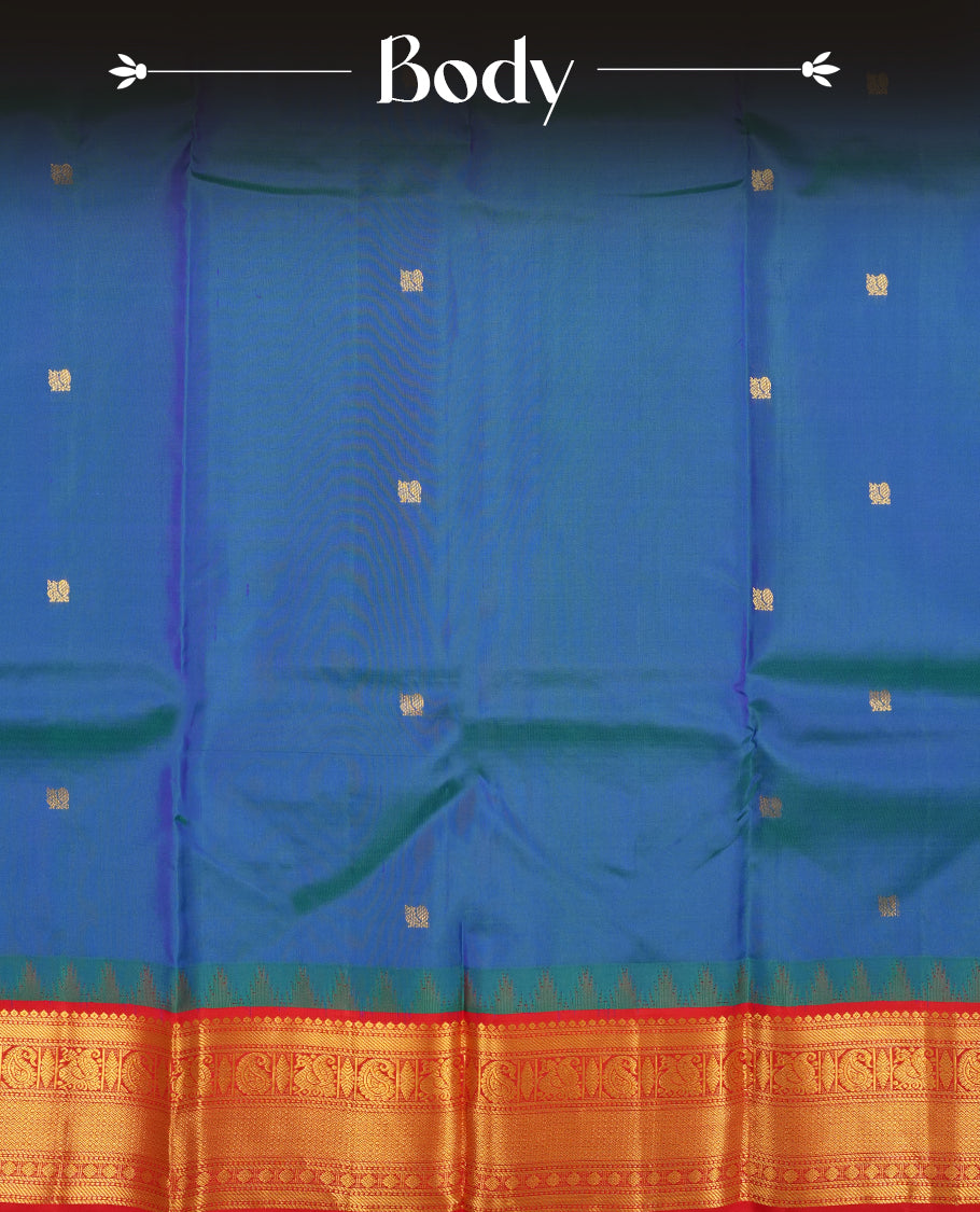 Peacock colour Vasundhara silk saree adorned with all-over gold mayil motifs on the body, complemented by a contrast red colour with gold traditional with mayil pattern border and paired with a matching blouse piece.