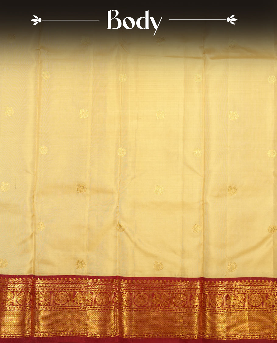Cream colour Vasundhara silk saree adorned with all-over gold chakkaram & mayil motifs on the body, complemented by a contrast maroon gold tarditional border and paired with a matching blouse piece.