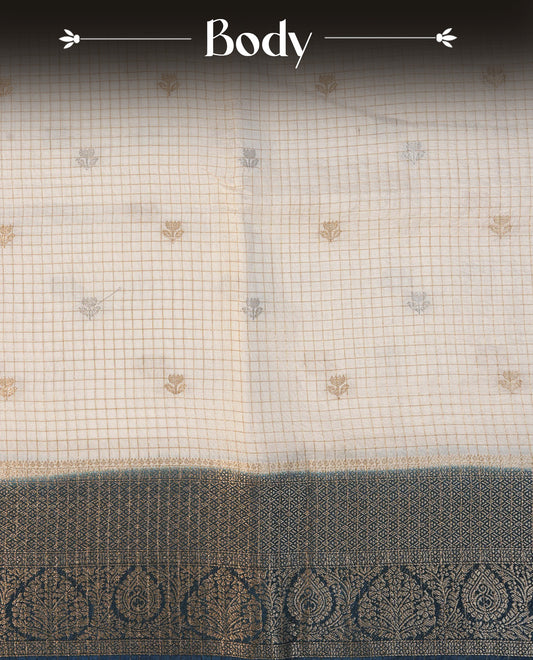 Semi Banaras Tussar Saree Featuring Gold Zari Check With Floral Pattern On Body , Teal Blue Colour  With Gold Zari Border , Paired With  A Matching Blouse Piece.