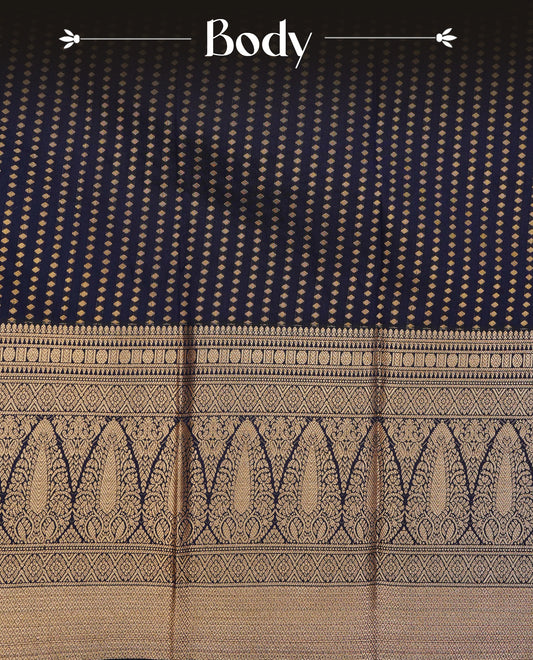 Dark navy blue colour soft silk saree featuring gold zari buttas on body, contrast self colour gold zari motifs on border, grand pallu comes with matching blouse piece.
