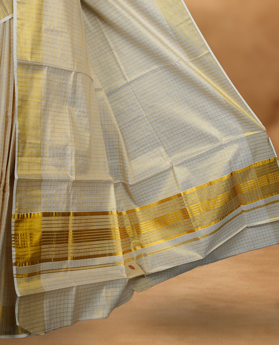 Off white colour Tissue Kerala saree featuring a subtle checked body, a refined golden zari border, and a traditionally woven pallu, paired with a matching blouse.