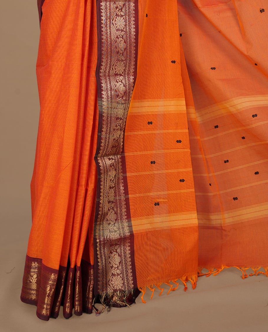 Orange colour chettinad cotton featuring black thread motifs on body, complemented by contrast brown colour with gold zari border, paired with matching blouse piece.