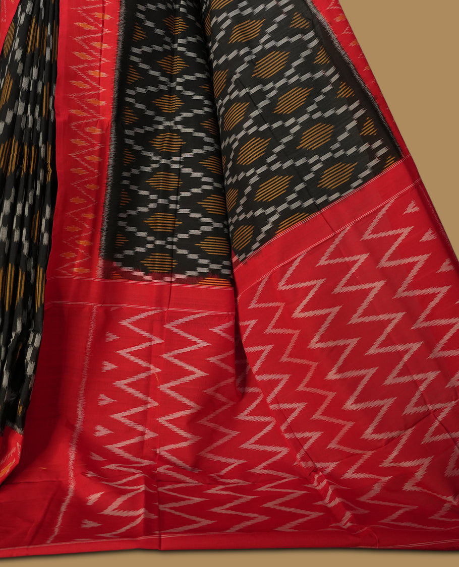 Black colour Ikkat Pochampally saree featuring a vibrant red border and pallu adorned with traditional ikat motifs in shades of beige & grey, bringing a perfect blend of heritage and modern charm.