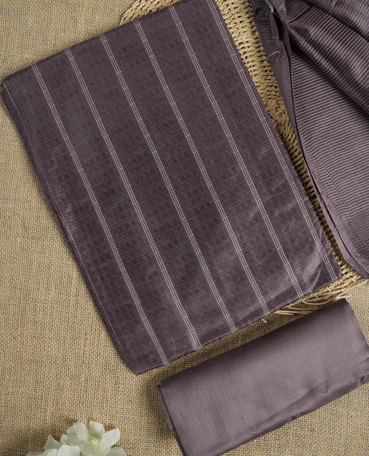 Dark pastel purple colour tussar suit material featuring a subtle self woven pattern and vertical lines on the body, paired with a lightweight matching dupatta with tassel edges and a plain bottom piece.