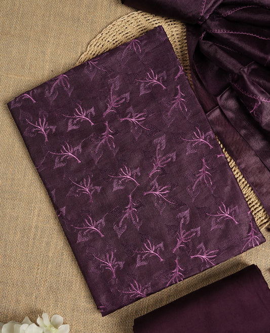 Dark grape colour tussar suit material featuring elegant floral thread embroidery on the body, paired with a soft dupatta adorned with matching embroidered motifs and tassel edges, along with a plain bottom piece.