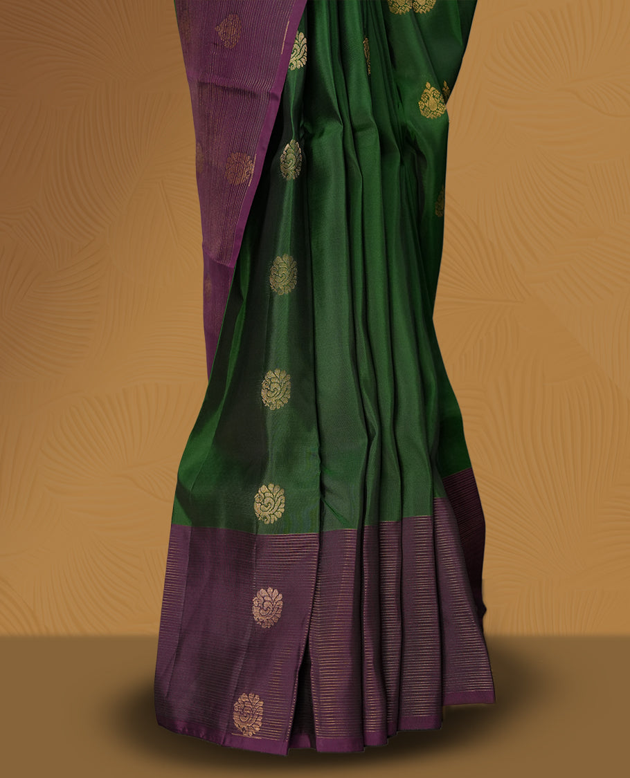Green colour soft silk saree adorned with golden buttas, complemented by a rich purple border and pallu featuring intricate zari designs & Paired with a matching blouse.