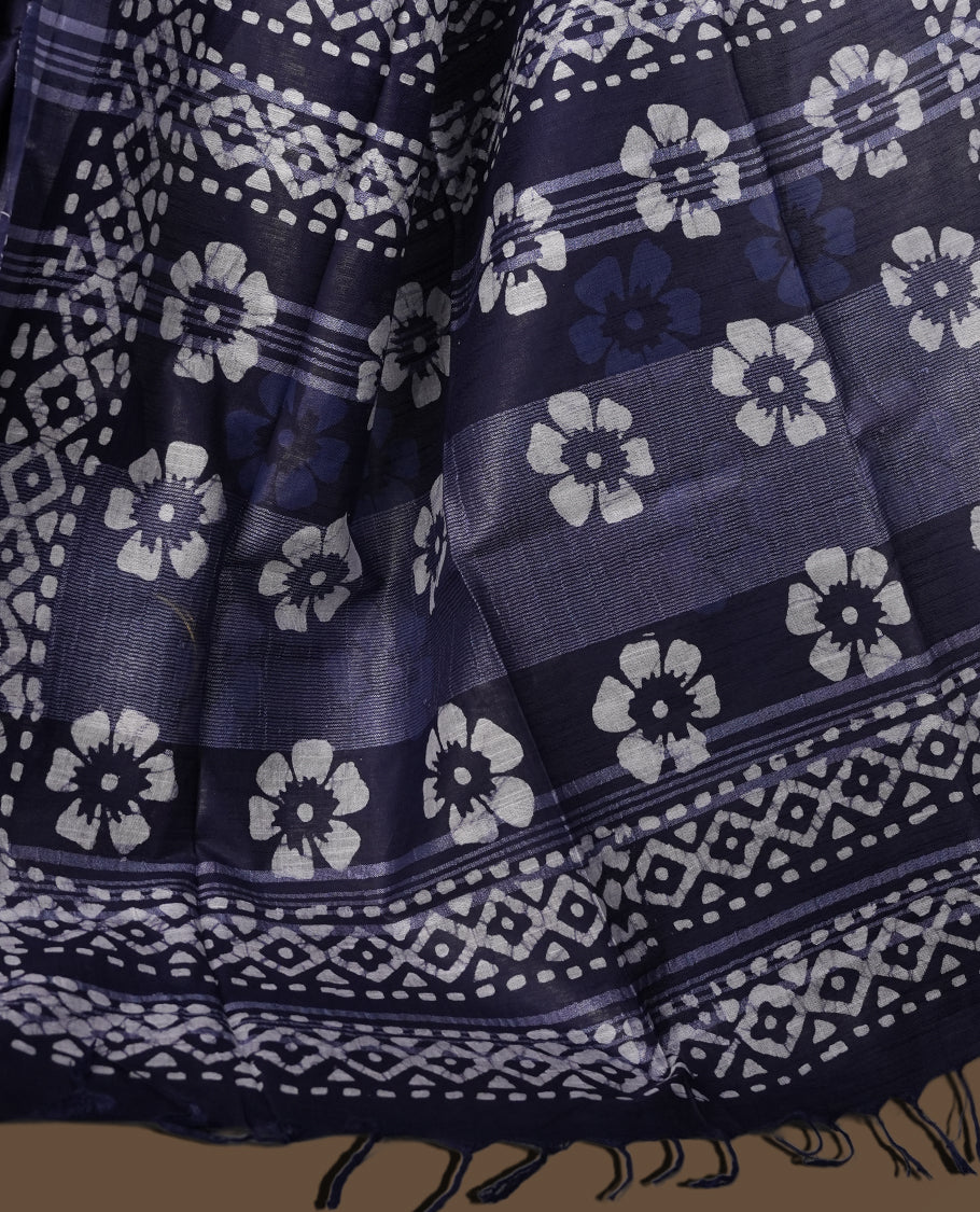 Navy blue colour semi jute tissue saree featuring white floral prints across the body, adorned with intricate geometric woven borders and a graceful floral work pallu & Comes with a matching blouse piece.