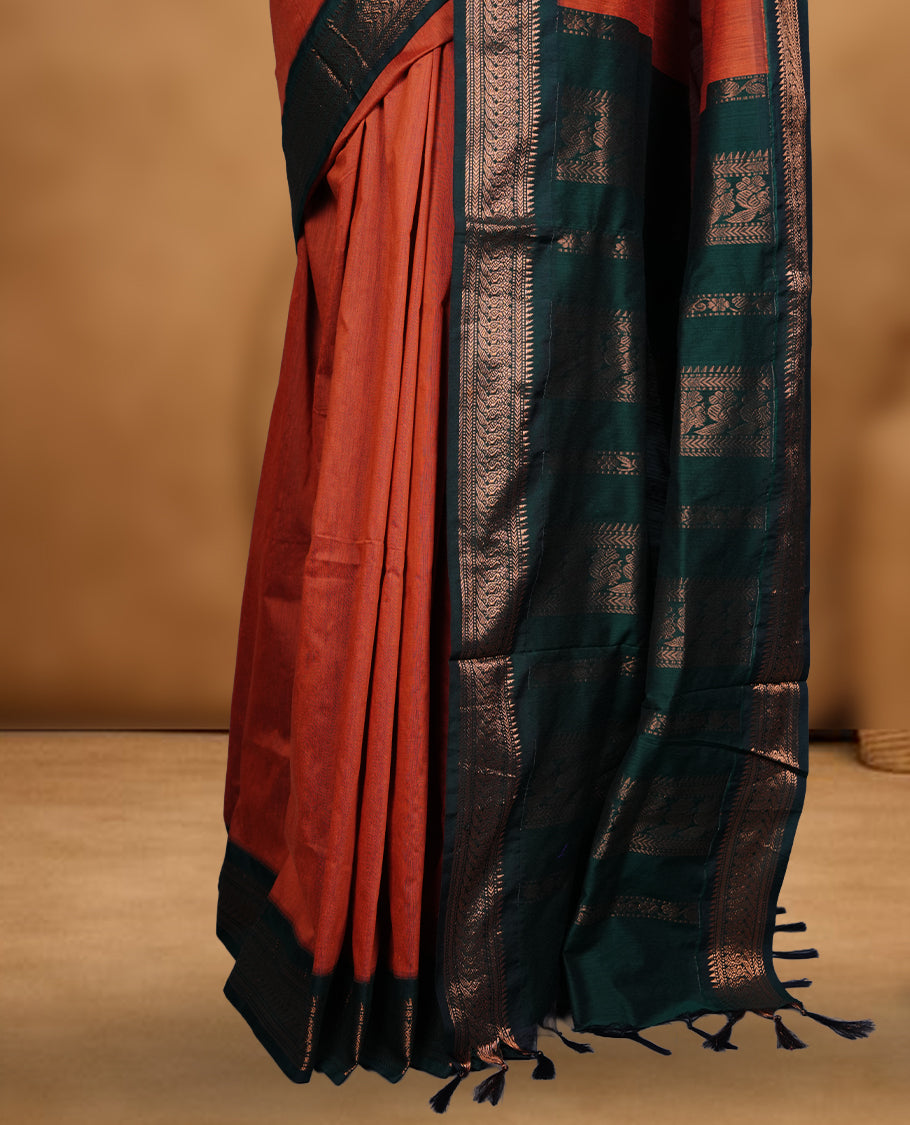 Rust orange colour Kalyani cotton saree featuring a plain elegant body, complemented by a rich dark green zari border and traditional woven pallu, paired with a matching blouse.