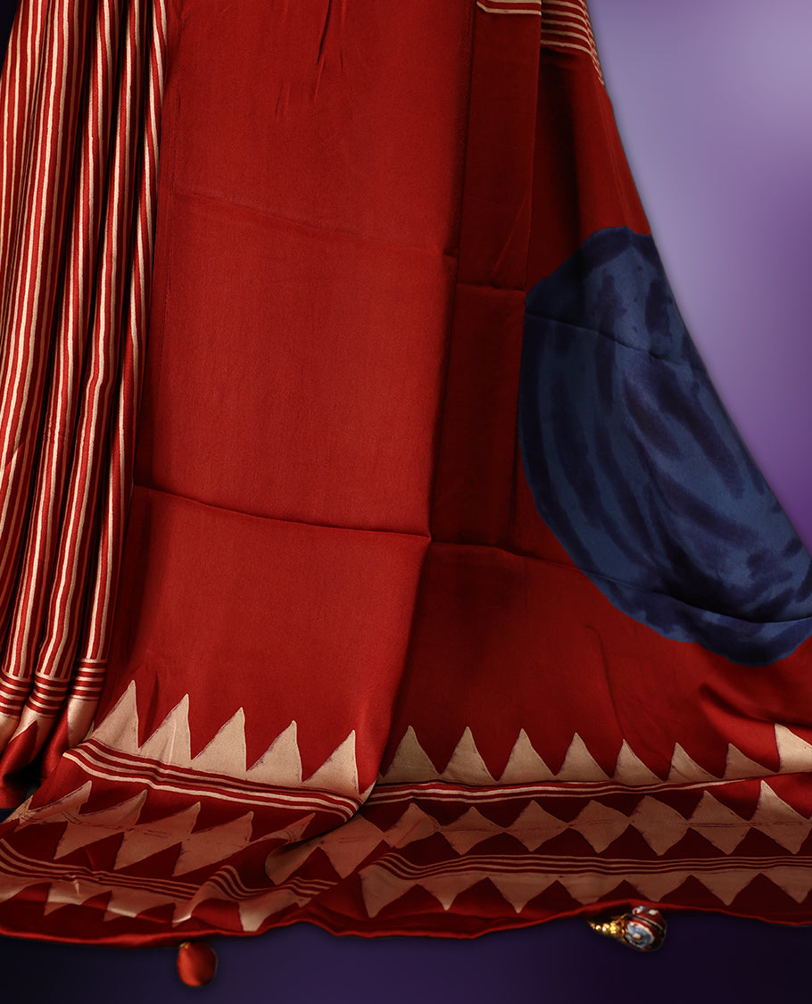 Maroon colour saree featuring bold striped patterns across the body, accentuated with a striking triangular border, and a contrasting pallu with geometric detailing, paired with a matching blouse