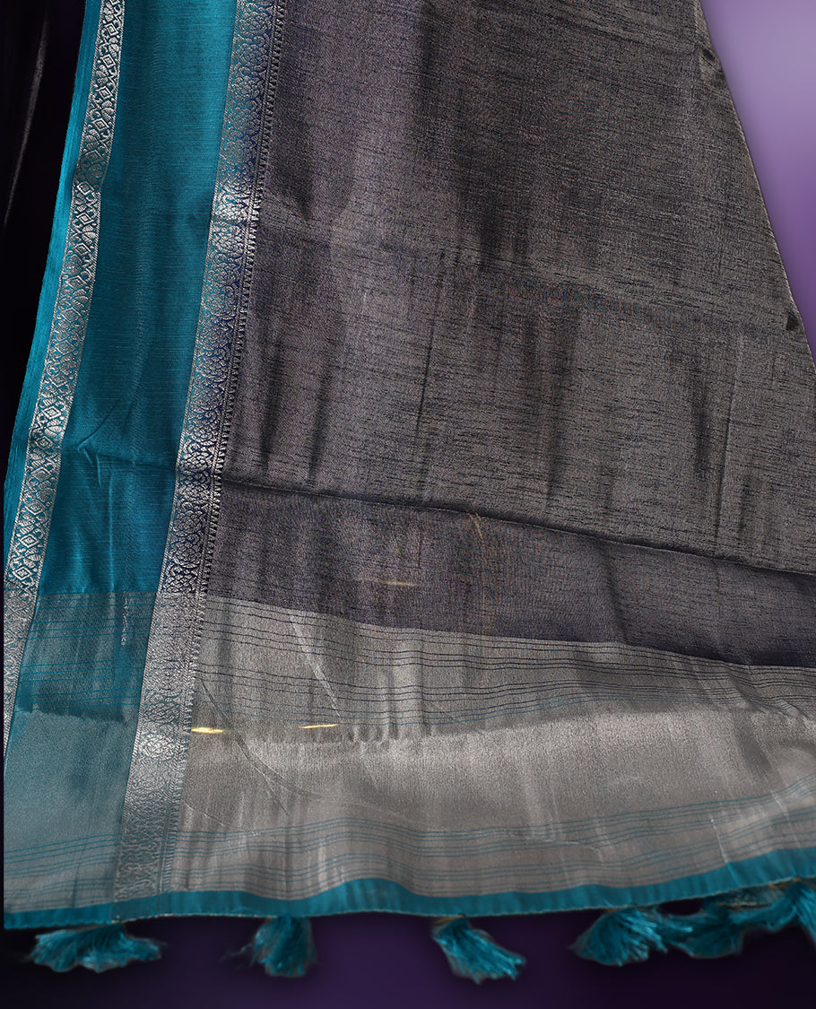 Steel grey saree with a rich sheen, paired with a contrasting turquoise blue border and pallu featuring delicate silver zari work, finished with tassels at the edge. Comes with a matching blouse piece.