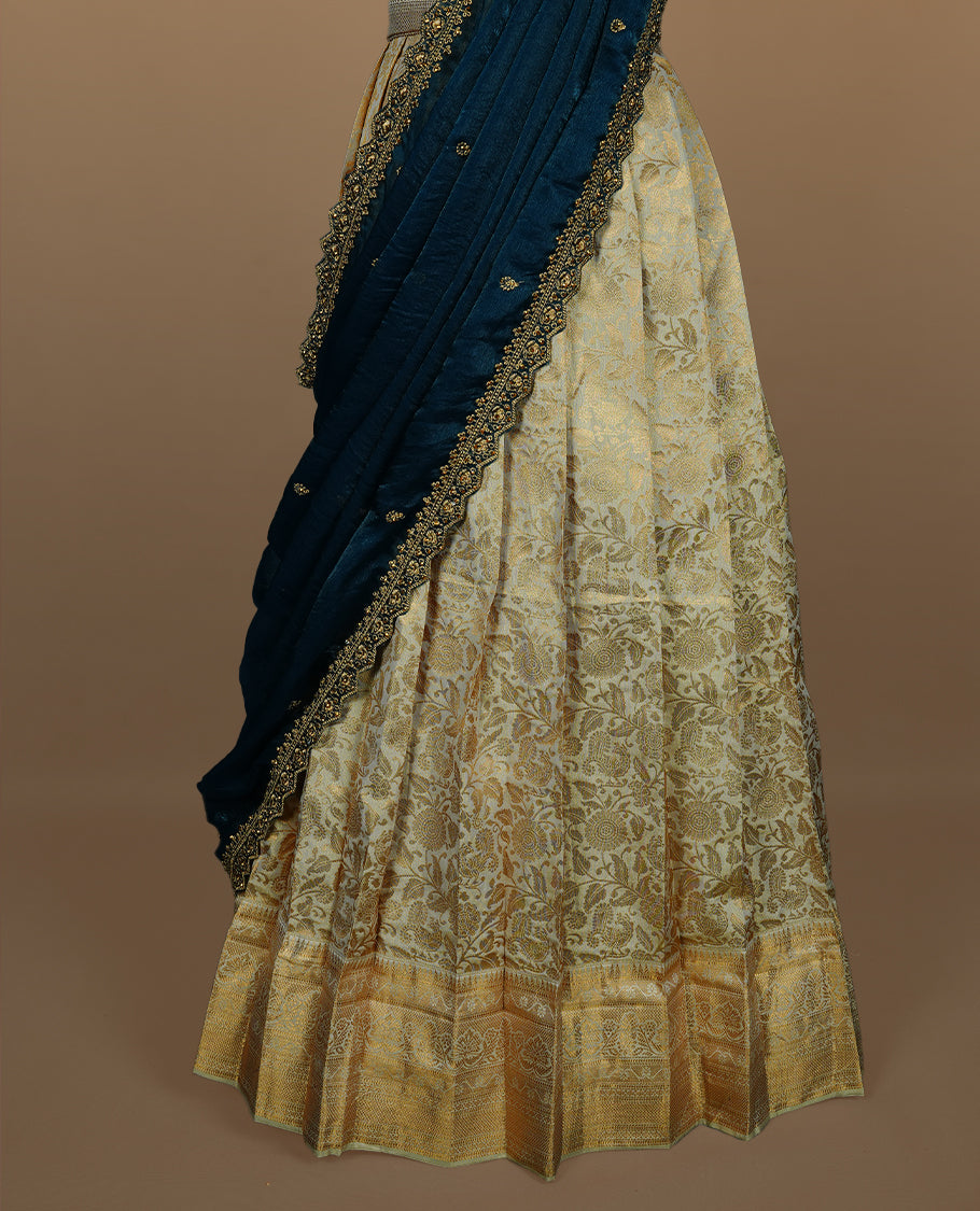 Light gold colour semi banaras semi stitched dhavani set featuring gold zari floral kodi motifs and traditional border, unstitched matching blouse piece and contrast Teal colour Duptta with gold thread and beats worked border.