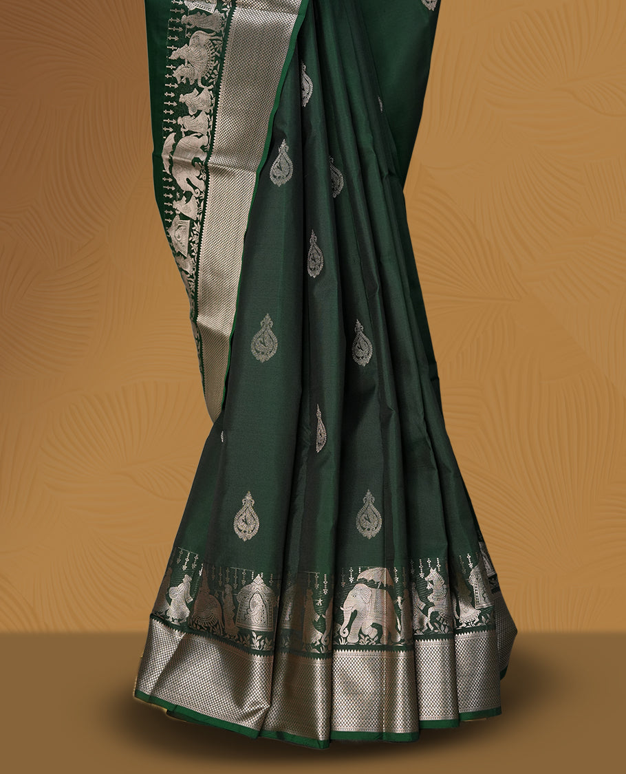 Dark green colour soft silk saree adorned with copper shade buttas, accentuated by a contrasting copper zari border and pallu with intricate motifs & Paired with a matching blouse.