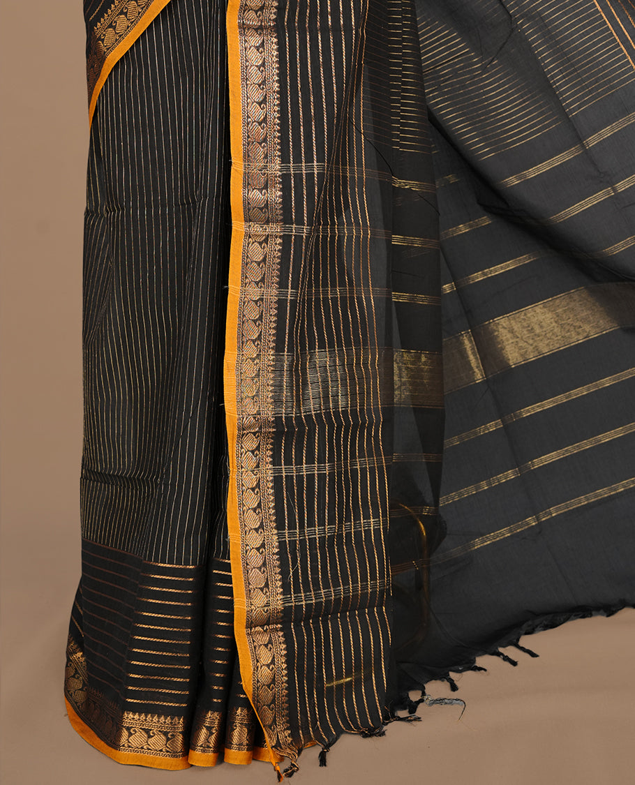 Black colour chettinad cotton saree featuring gold zari stripes on body, complemented by yellow piping with gold zari border, paired with matching blouse piece.