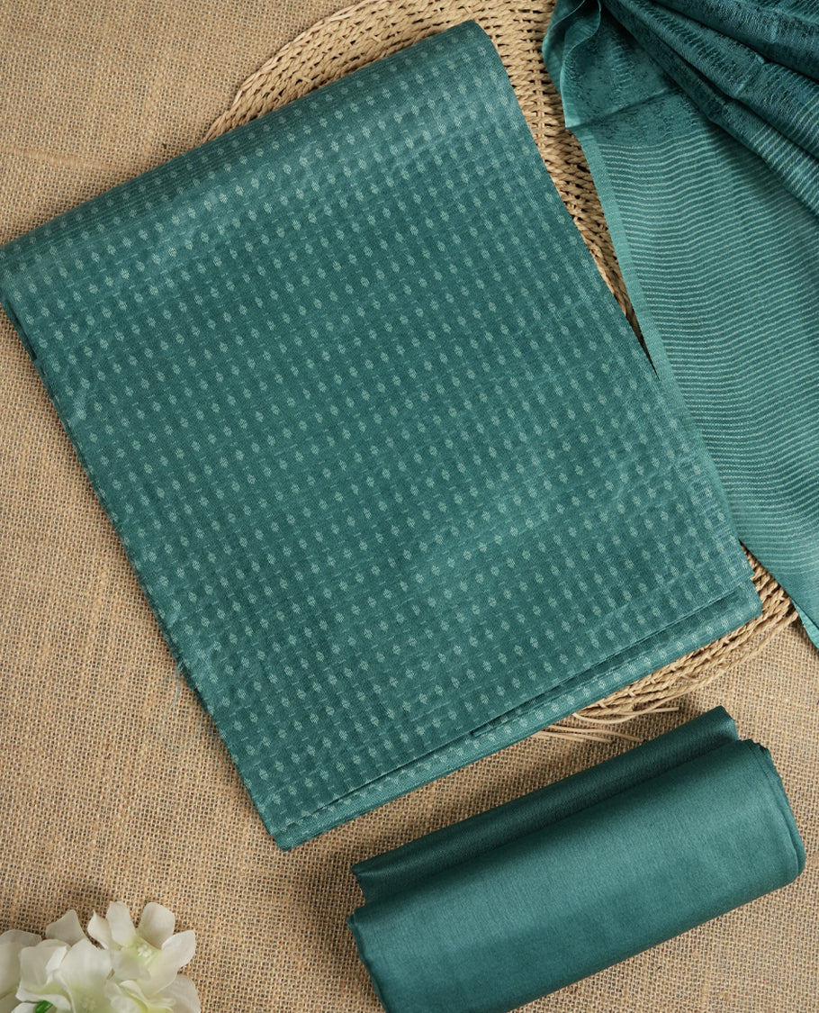 Teal blue colour tussar suit material featuring a subtle self woven textured body, paired with a soft striped dupatta detailed with tassel edges and a matching bottom piece.